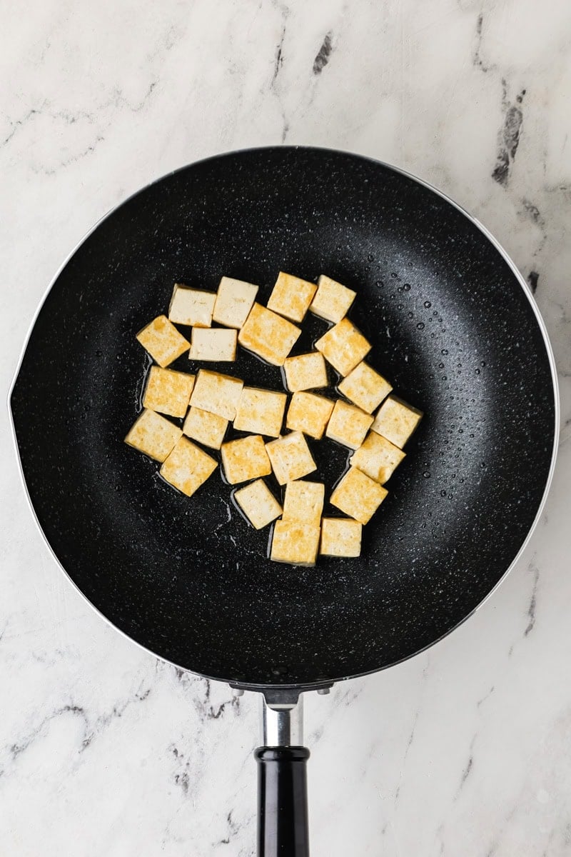 Tofu being fried in a pan.