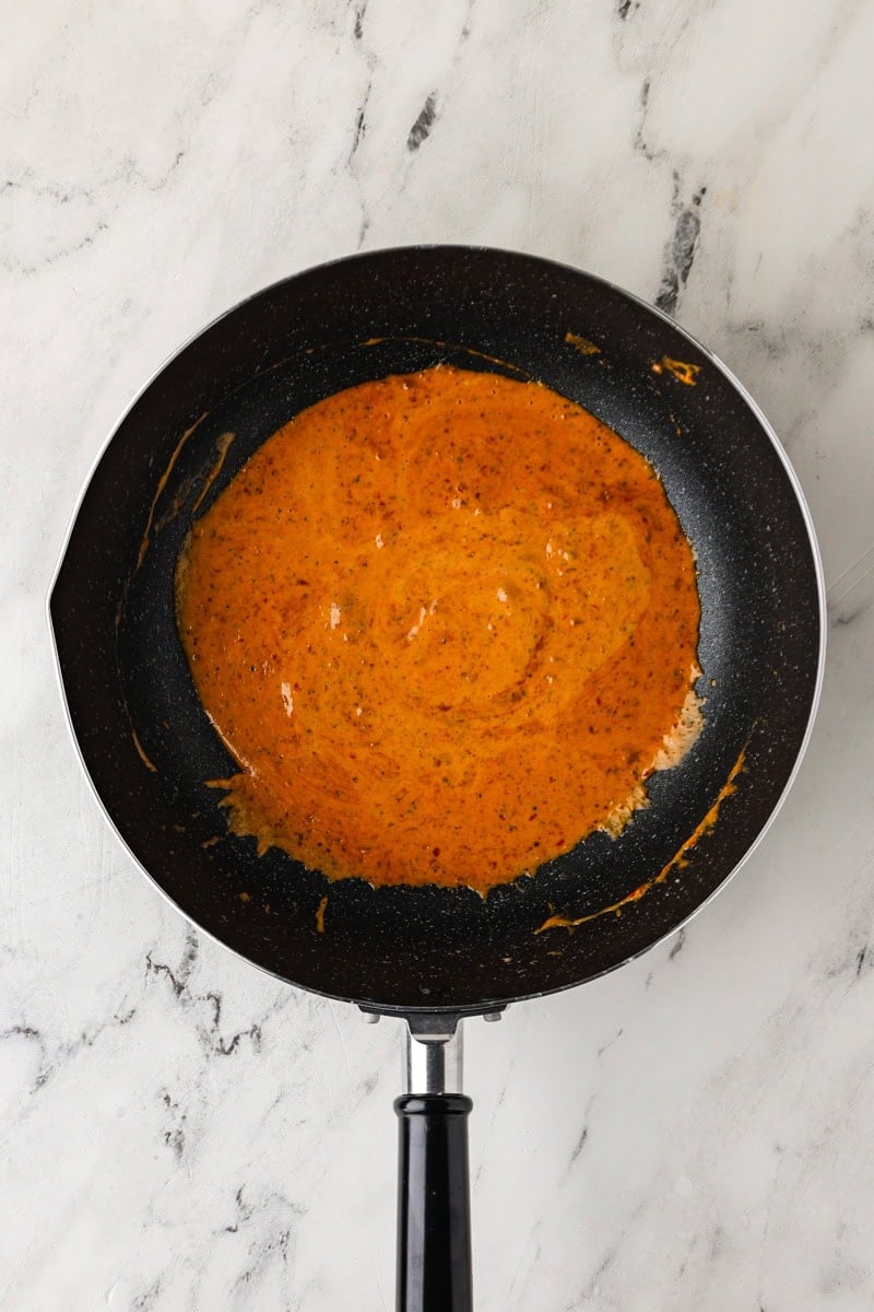 An overhead image of combining the thick part of coconut milk with red curry paste.