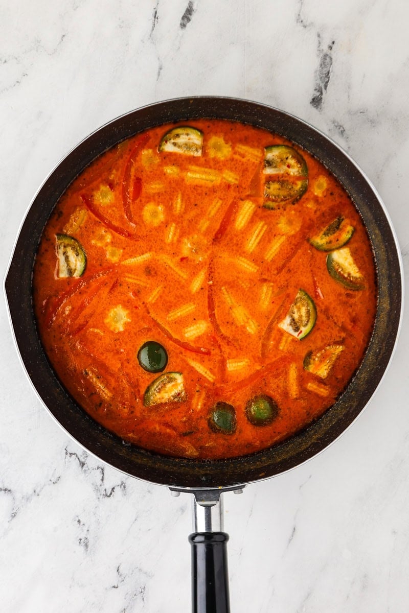 An overhead image of adding the eggplants, red bell pepper, and baby corn.