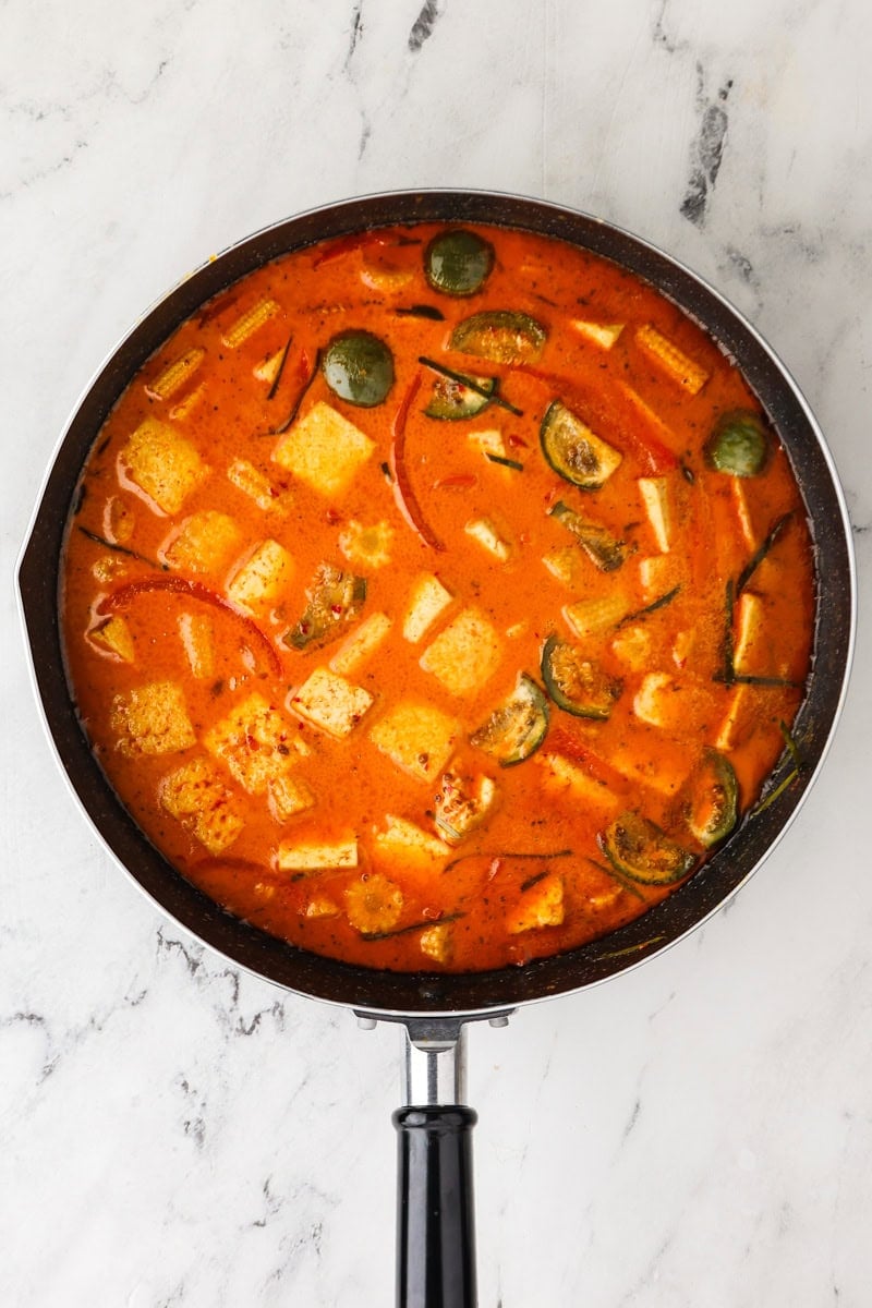 An overhead image of adding the tofu, makrut lime leaves, fish sauce, and coconut sugar.