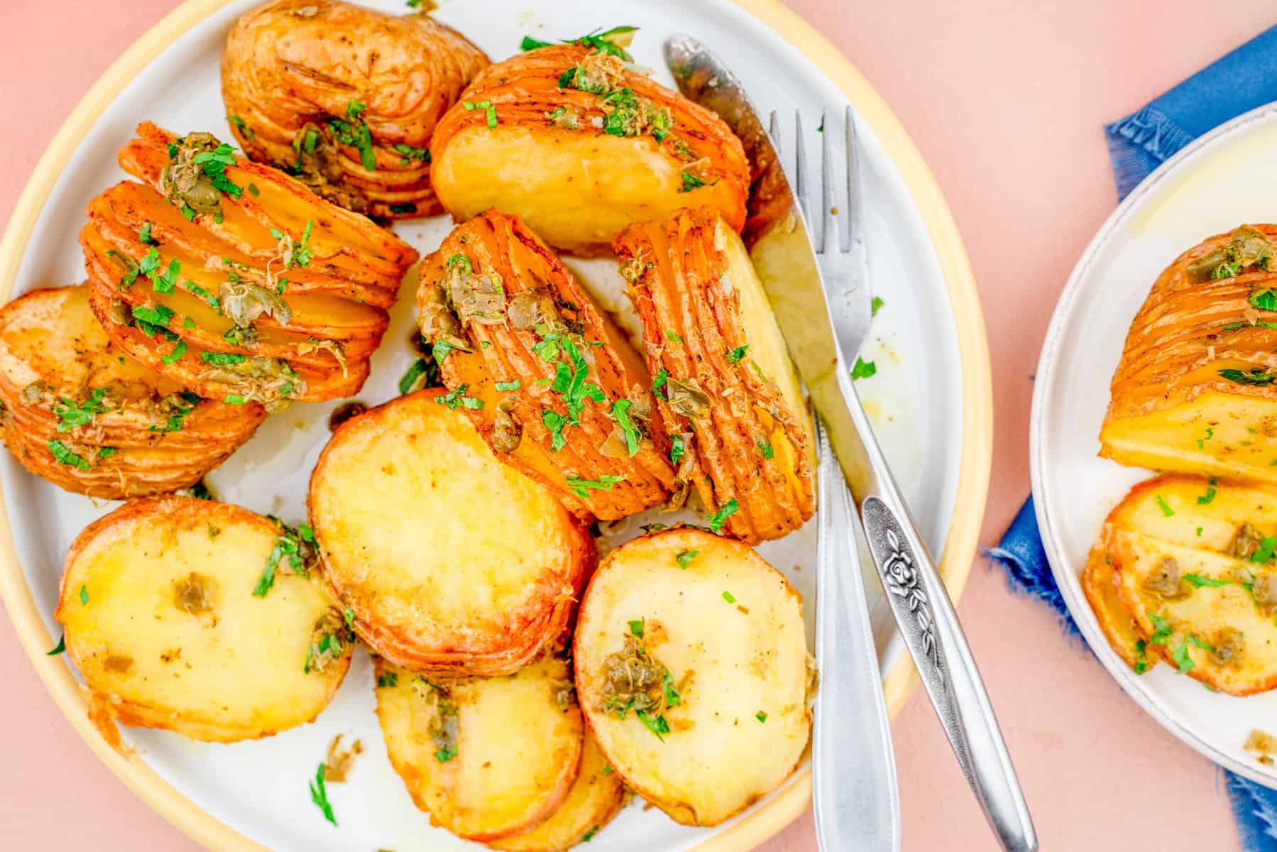 An overhead image of air fried hassel back potatoes on a plate with parsley on top and a fork and knife on the right side.