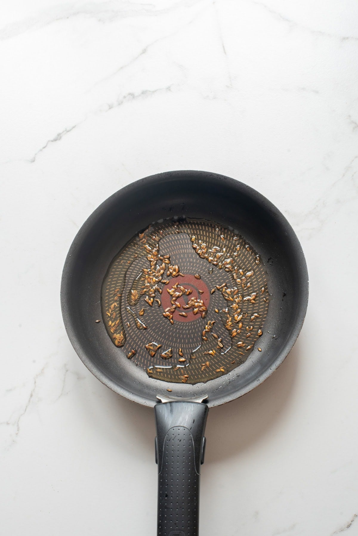 An overhead image of toasting cumin seeds on a skillet.