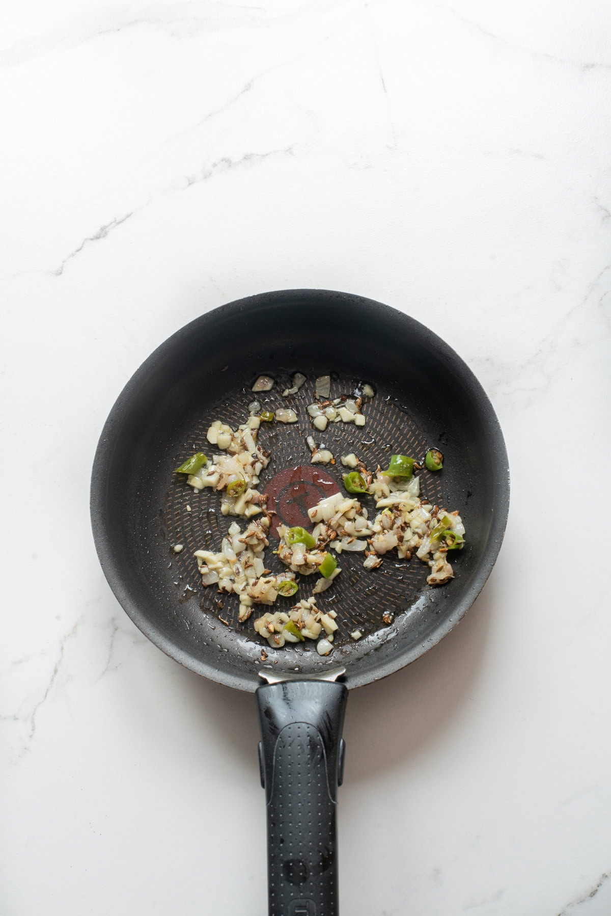 An overhead image of sauteing garlic, ginger, and serrano pepper on a pan.