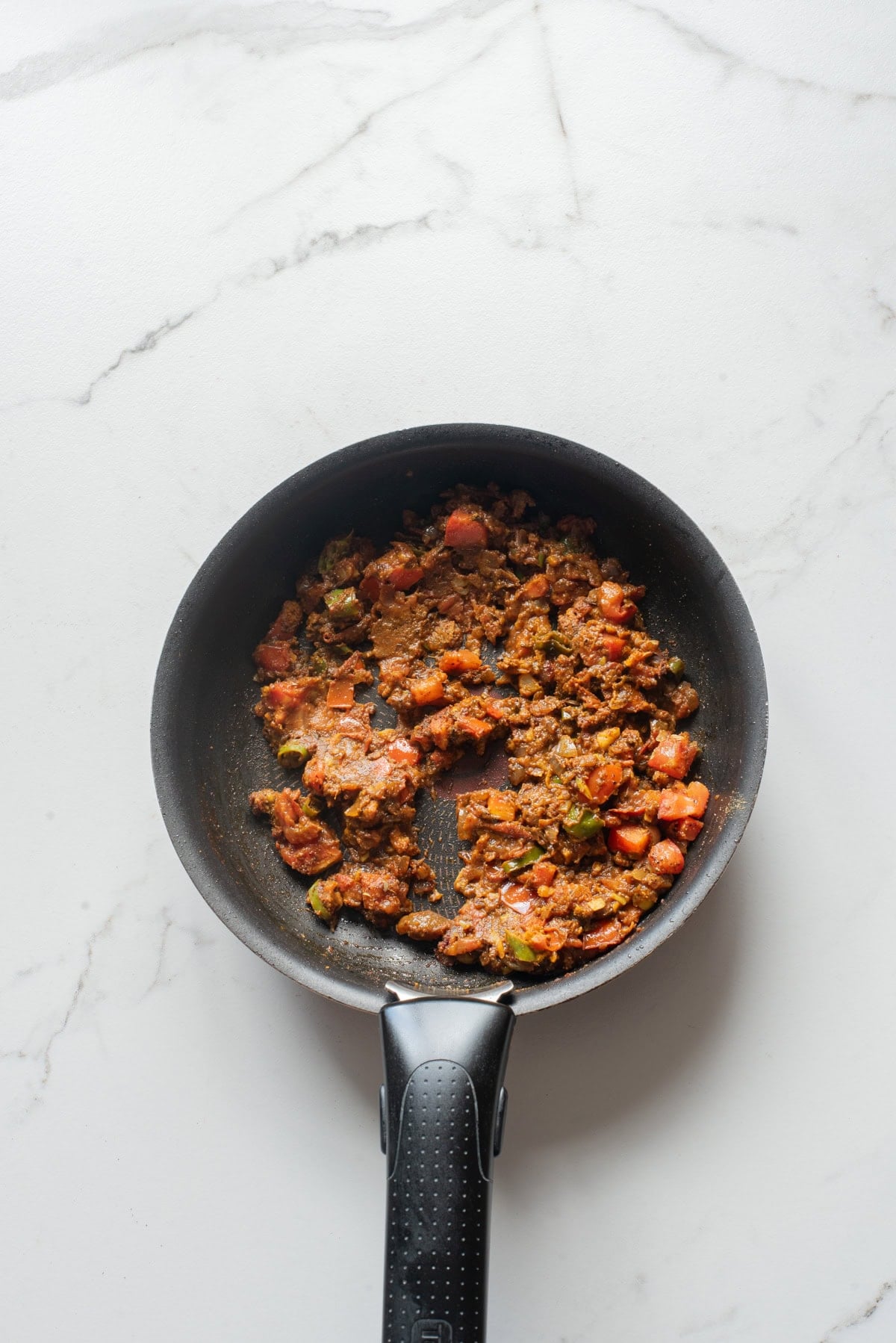 An overhead image of adding tomatoes and spices on a pan.