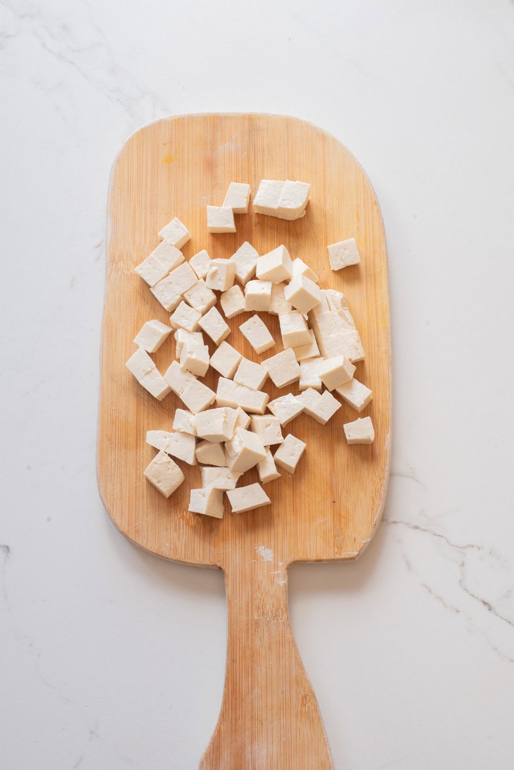 Tofu cut in cubes on a wooden board.