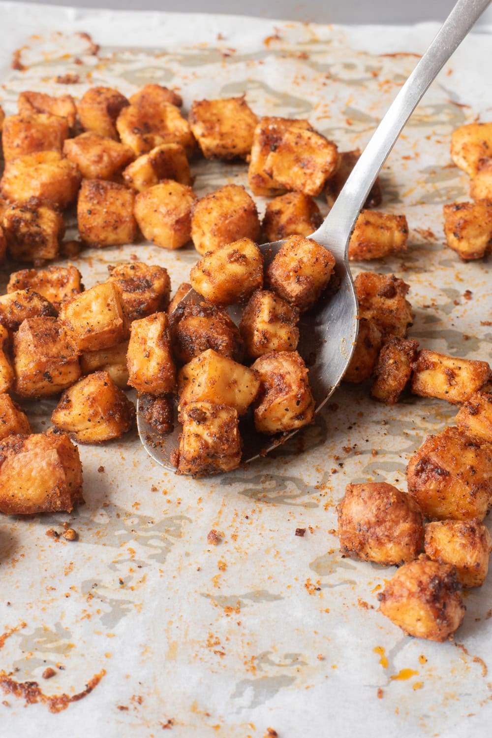 Golden crispy tofu croutons on a baking sheet with a spoon lifting a portion.