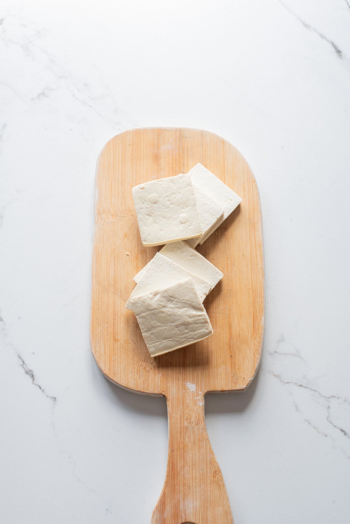 An overhead image of tofu cubes on a wooden cutting board.