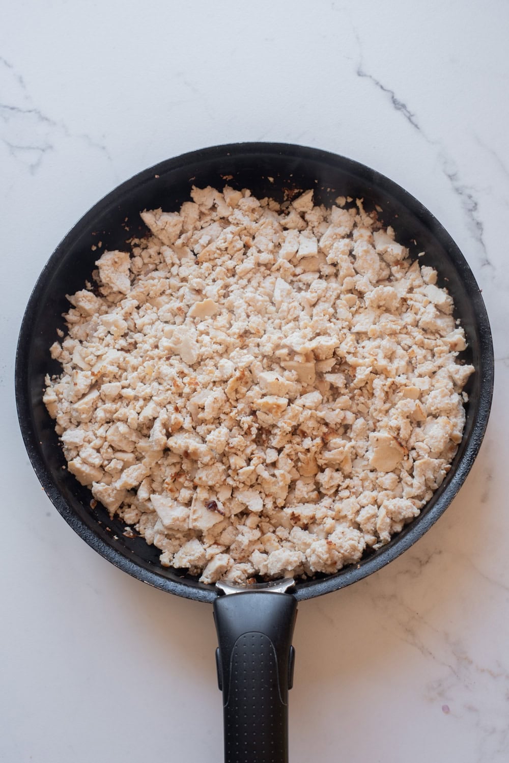 Crumbled tofu added to a skillet and cooking until lightly golden.