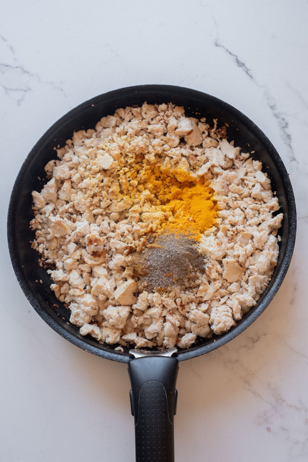 Turmeric, cumin, and seasonings added to tofu in a skillet.