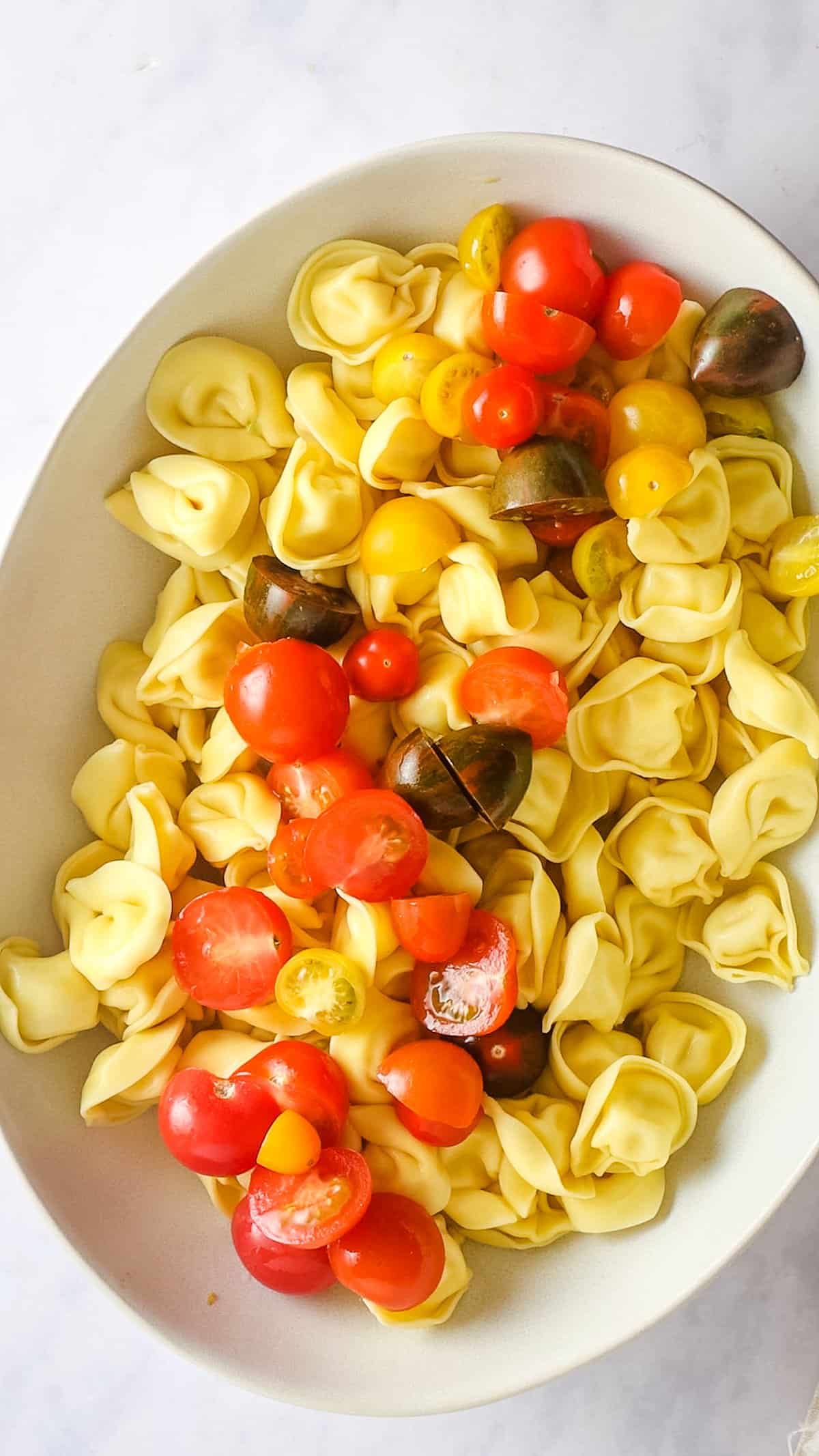 Overhead view of cherry tomatoes added to cooked tortellini