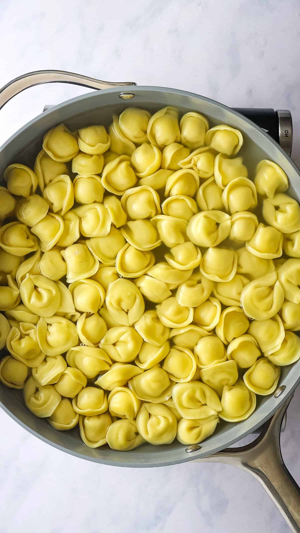 Overhead view showing tortellini cooking in a large skillet.