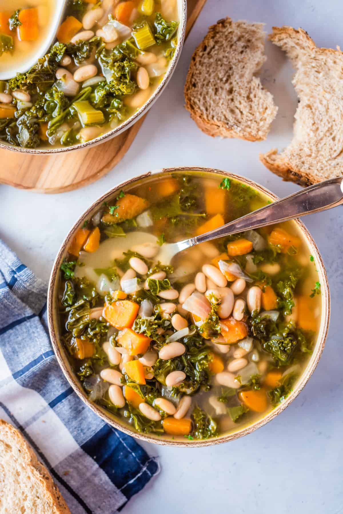 Overhead view of Tuscan bean soup with kale on a serving dish with a spoon on the side.