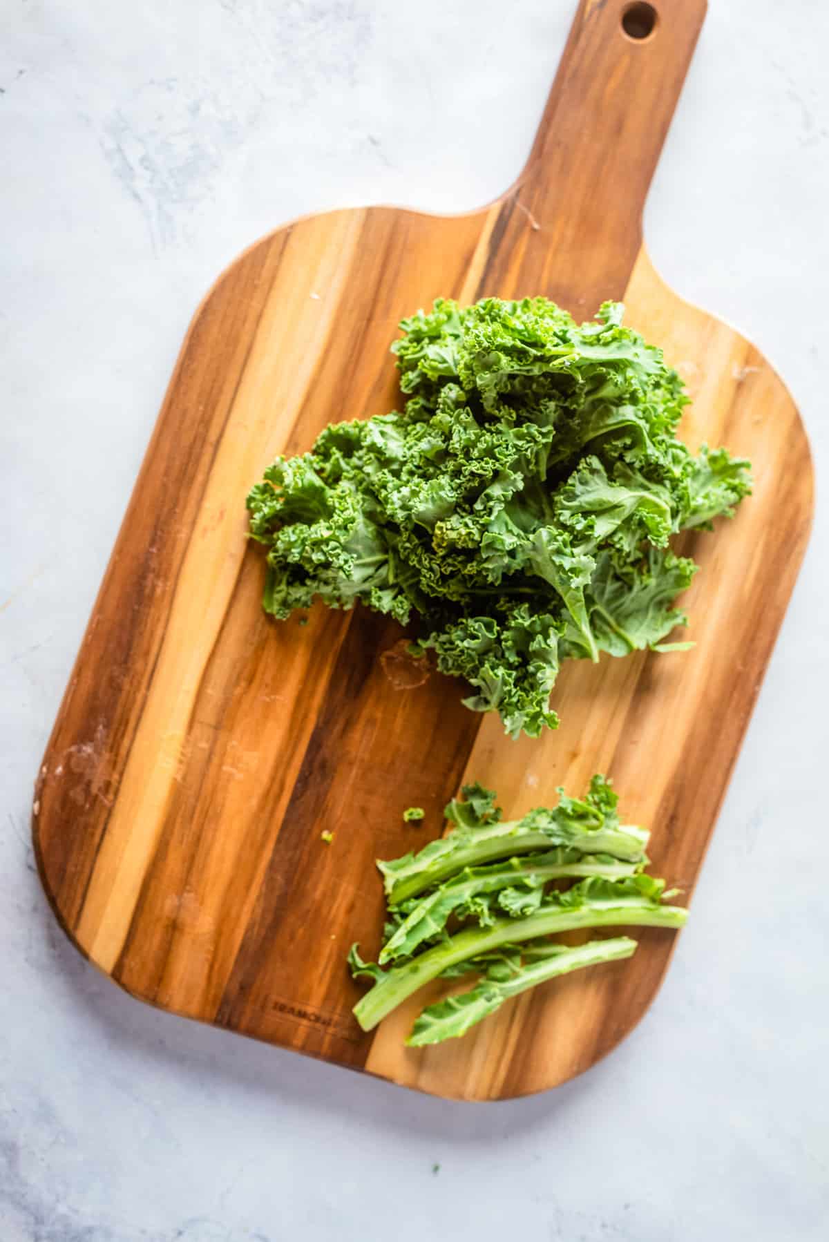 Overhead view of a wooden chopping board with chopped kale leaves and stem on top.