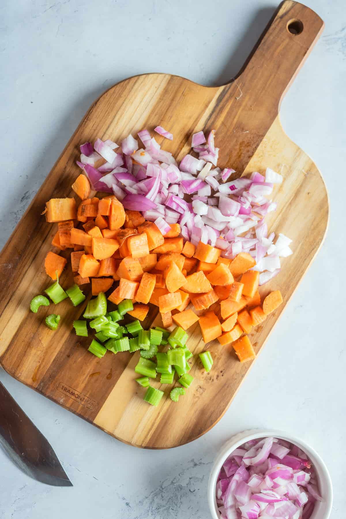Overhead view of chopped shallots, carrots, and celery on top of a wooden chopping board. 