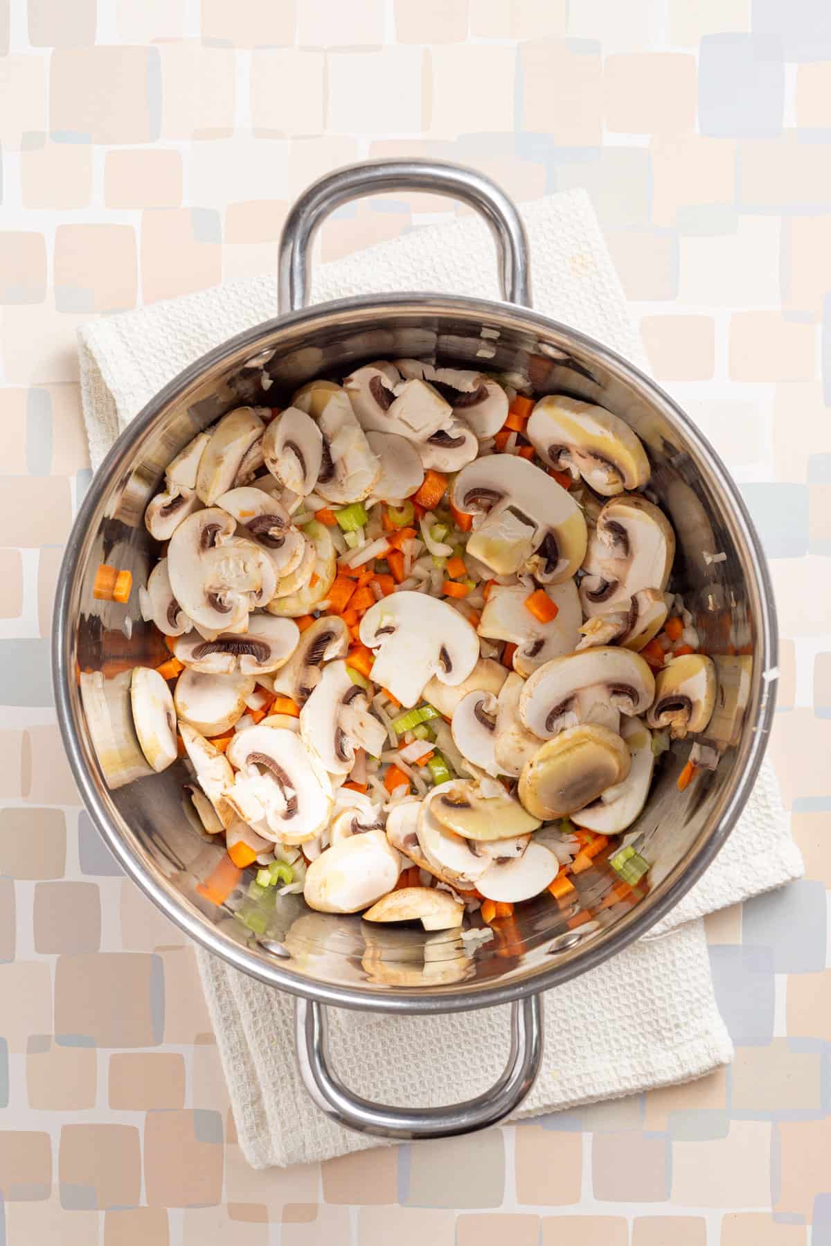 An overhead image of chopped onions, celery, mushrooms and carrots in a saucepan.