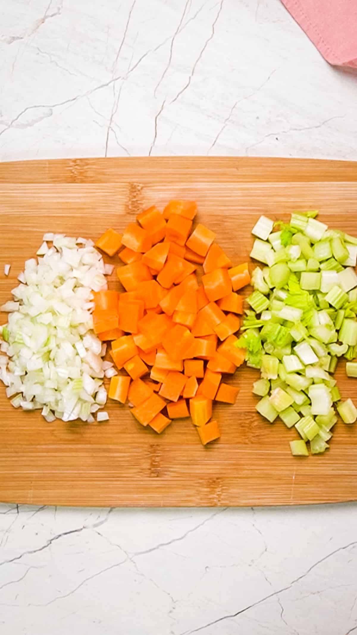 Overhead shot of onions, carrots and celery chopped into even pieces.