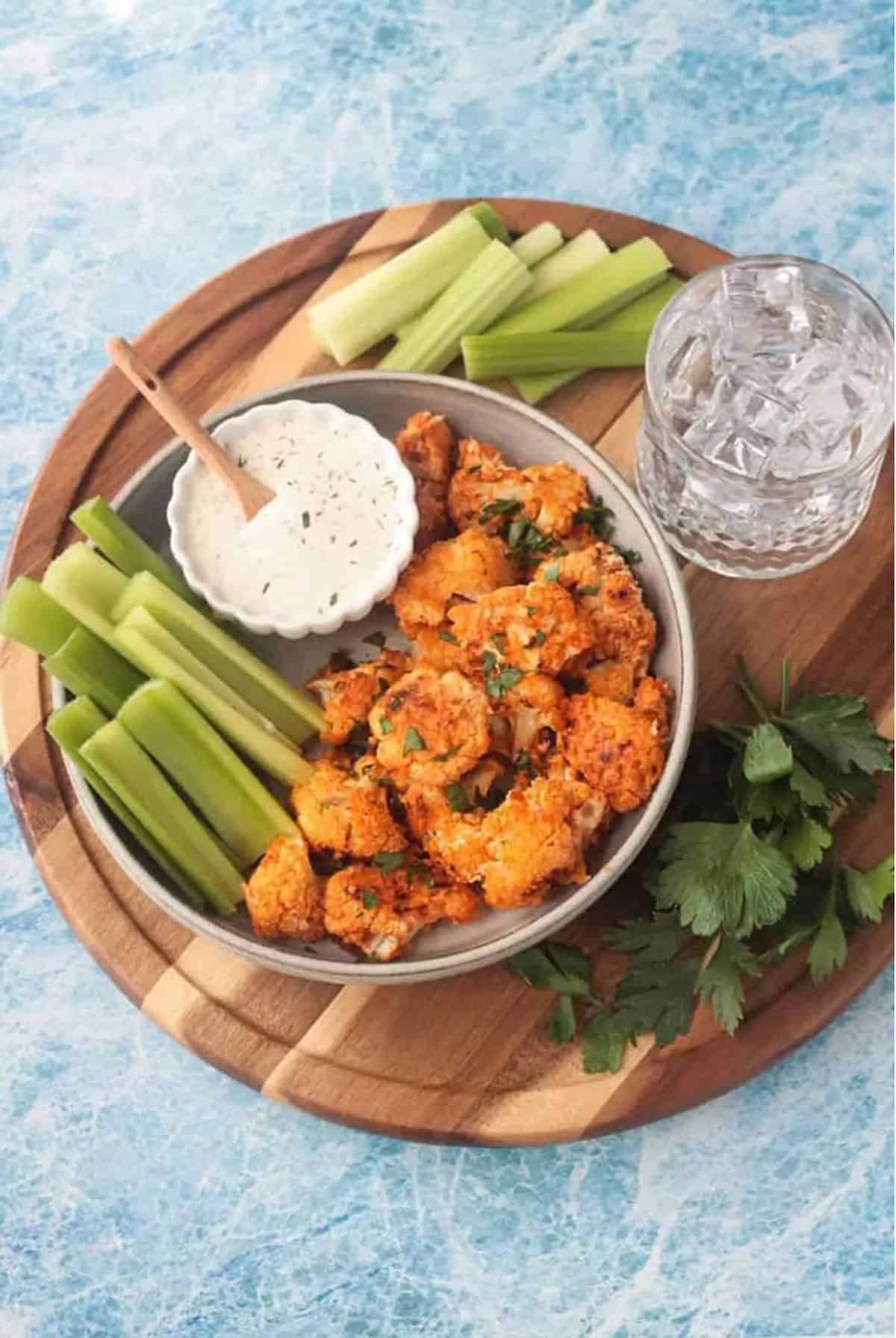 Cauliflower bites in a bowl with some celery sticks and ranch dressing