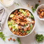 Overhead image of vegan Caesar salad with crispy tofu croutons and roasted chickpeas, served with creamy dressing and fresh parsley on the side.