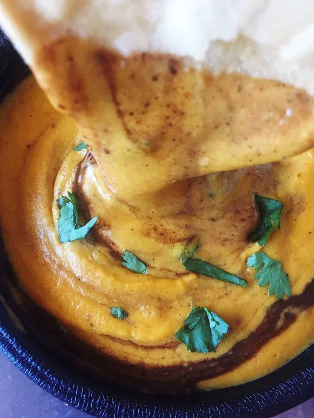 Close up of tortilla chip dipping into a vegan chili cheese sauce