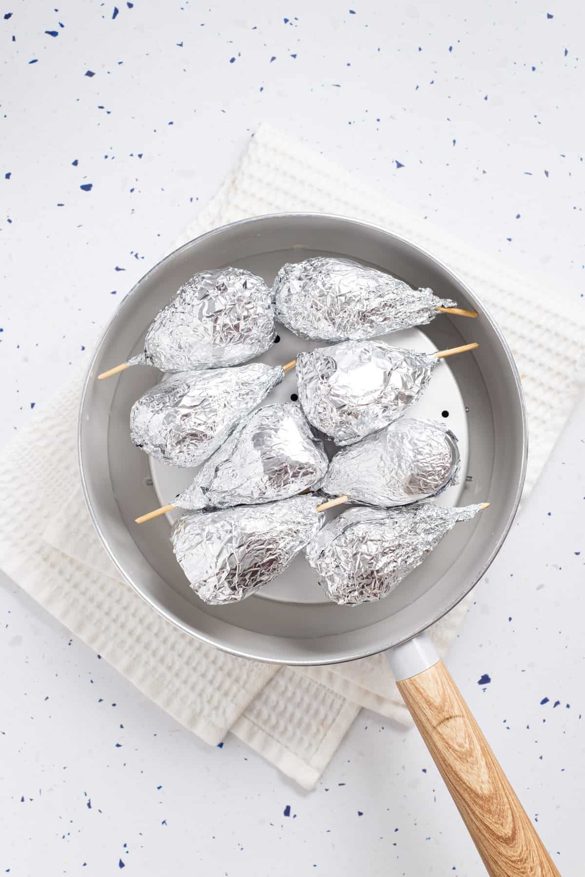Overhead view of uncooked vegan drumsticks wrapped in foil and placed on a steamer. 