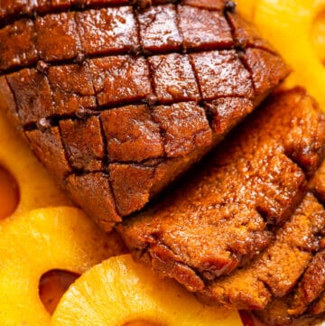 A close-up overhead view of a whole vegan ham with slices of it above pineapple slices.