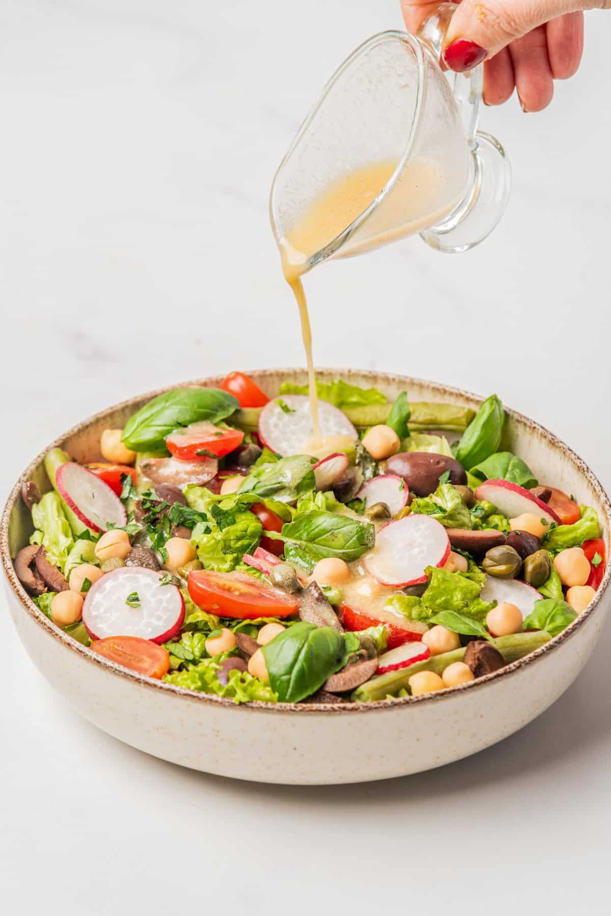 An image of vegan nicoise salad served on a big bowl while being drizzled by champagne vinaigrette.
