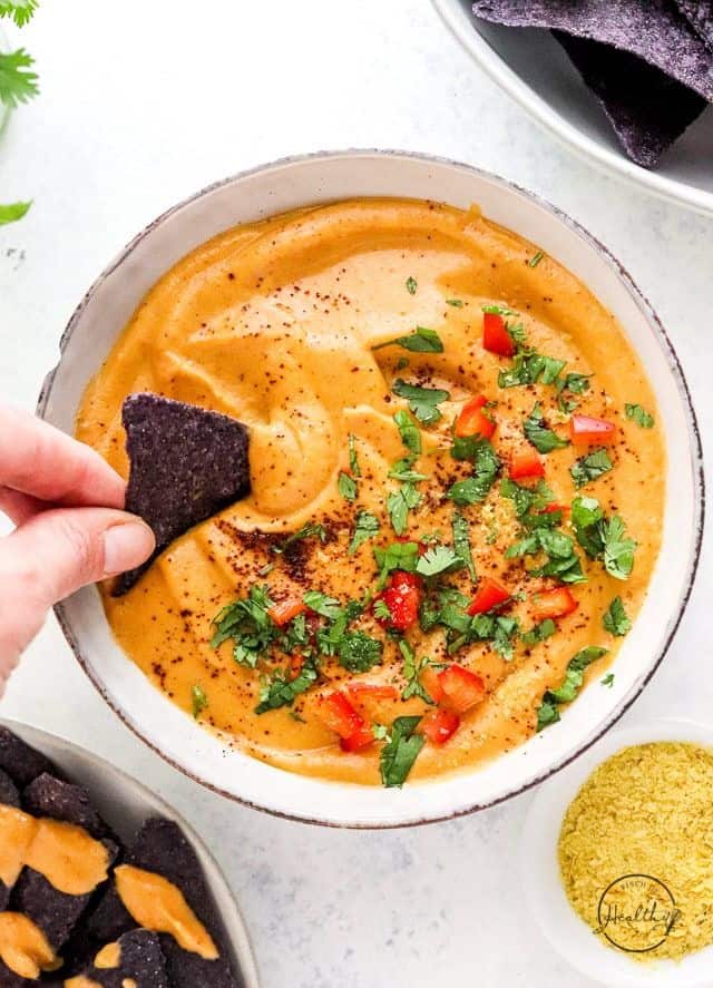 Close up of bowl of vegan queso with tortilla chip being dipped in