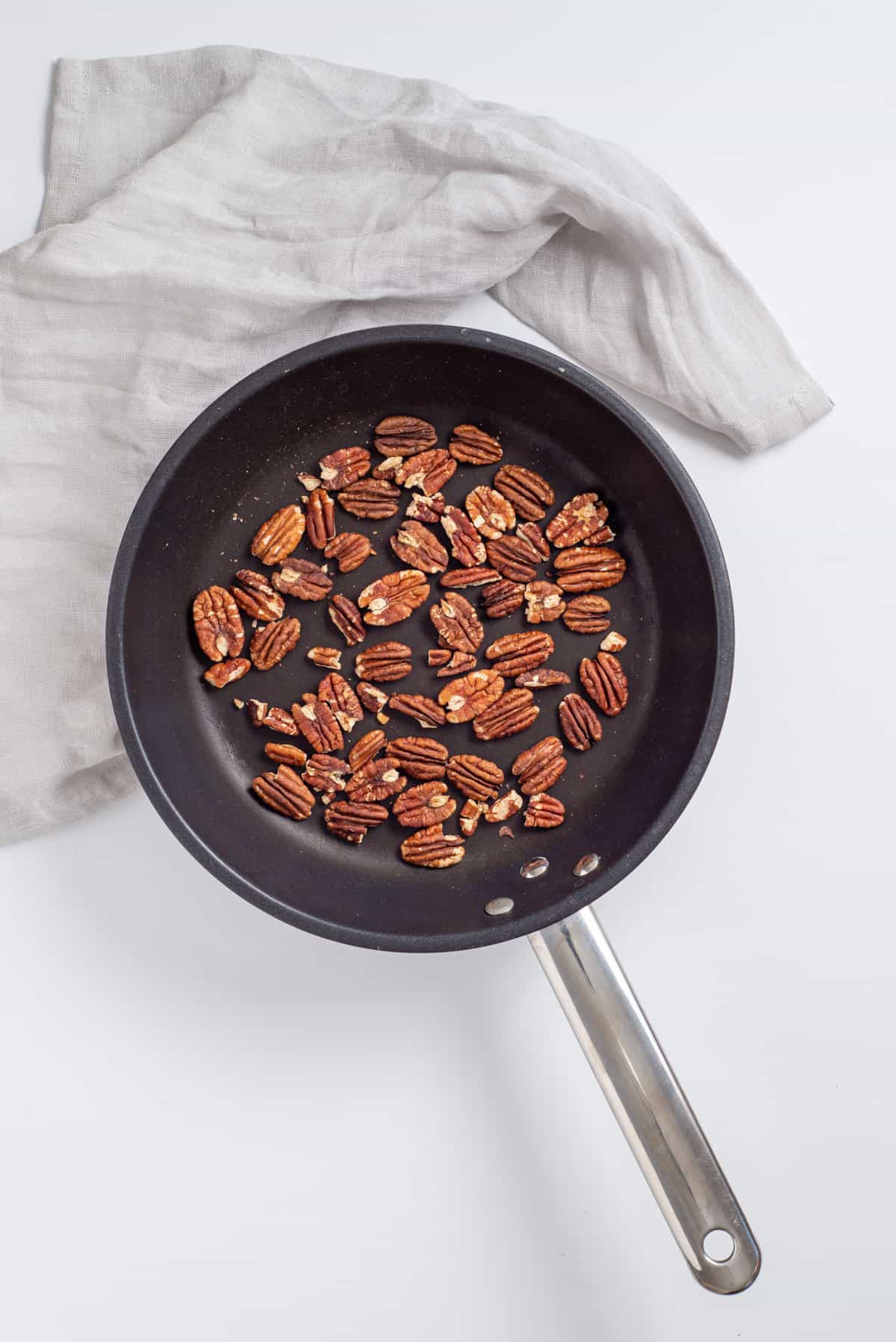 Overhead view of pecans being toasted in a large skillet.