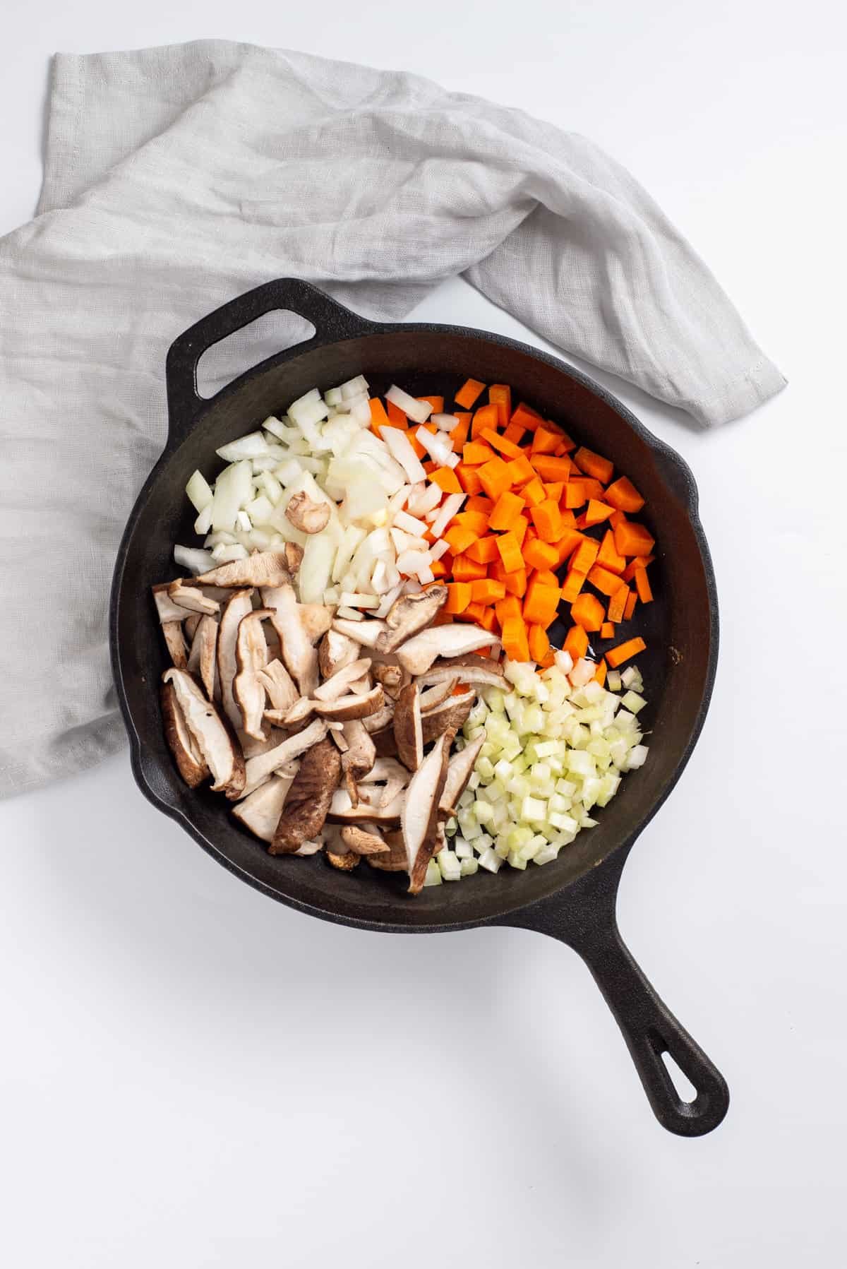Overhead view showing skillet with onions, carrots, celery and shiitake mushrooms.