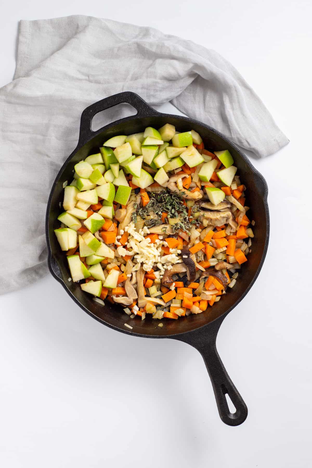 Overhead view of skillet with apples, herbs added in.