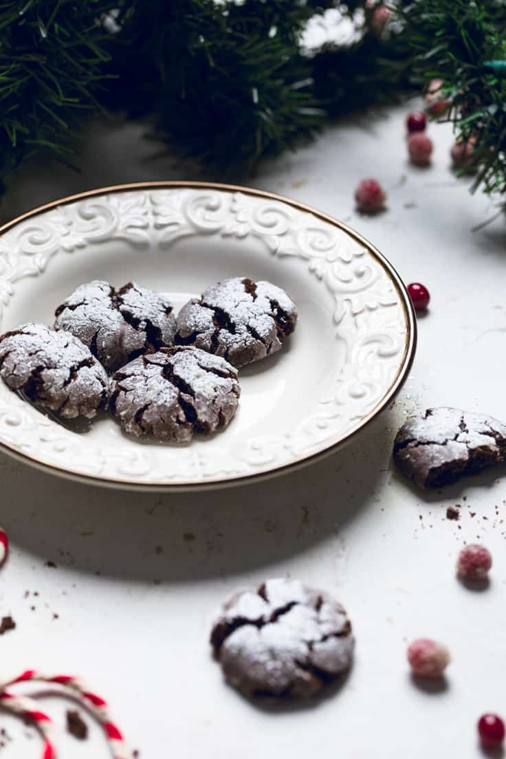 A straight view of vegan chocolate crinkle cookies placed in a white plate with half and whole crinkles on the side of the plate.
