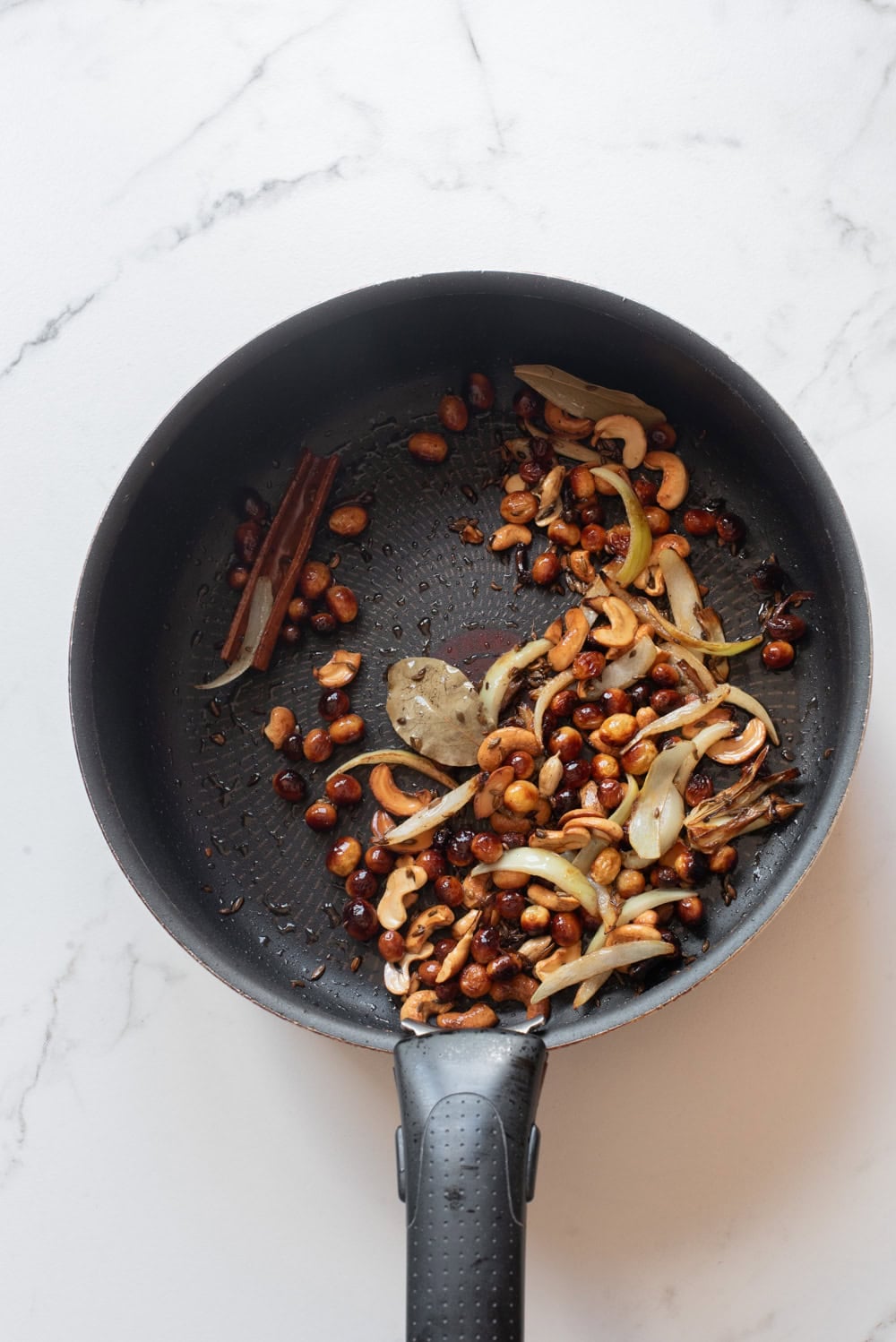 Whole spices, cashews, raisins, and onion cooking in ghee for vegetable biryani.