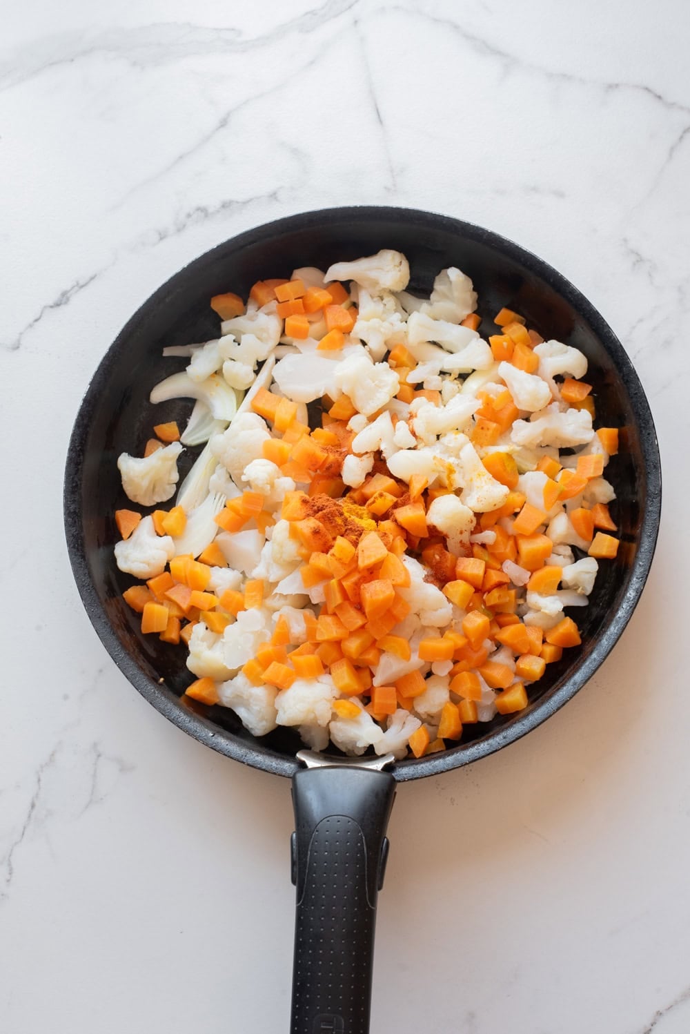 Cauliflower, carrots, onion, and ginger added in a skillet for vegetable biryani.
