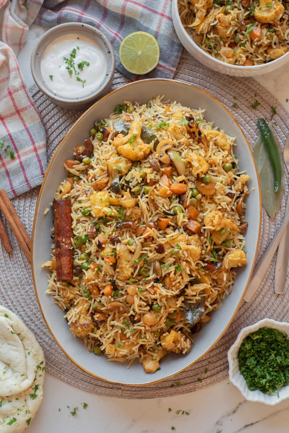Home-style vegetable biryani served on a platter with raita, naan, and fresh cilantro.