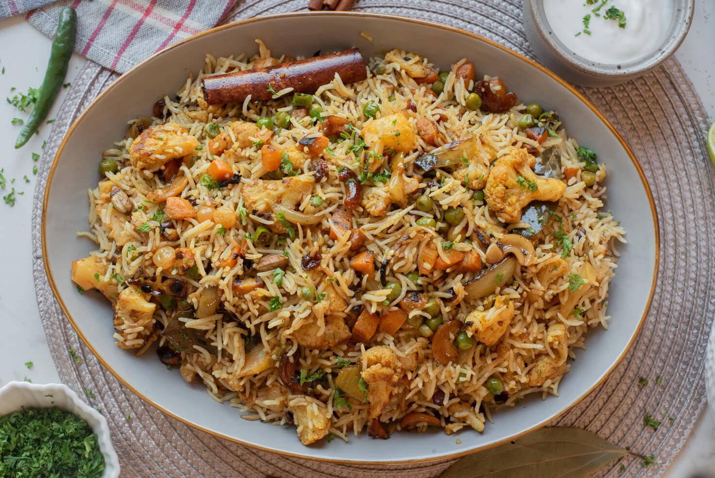 Vegetable biryani with cauliflower, carrots, peas, and whole spices served family-style.