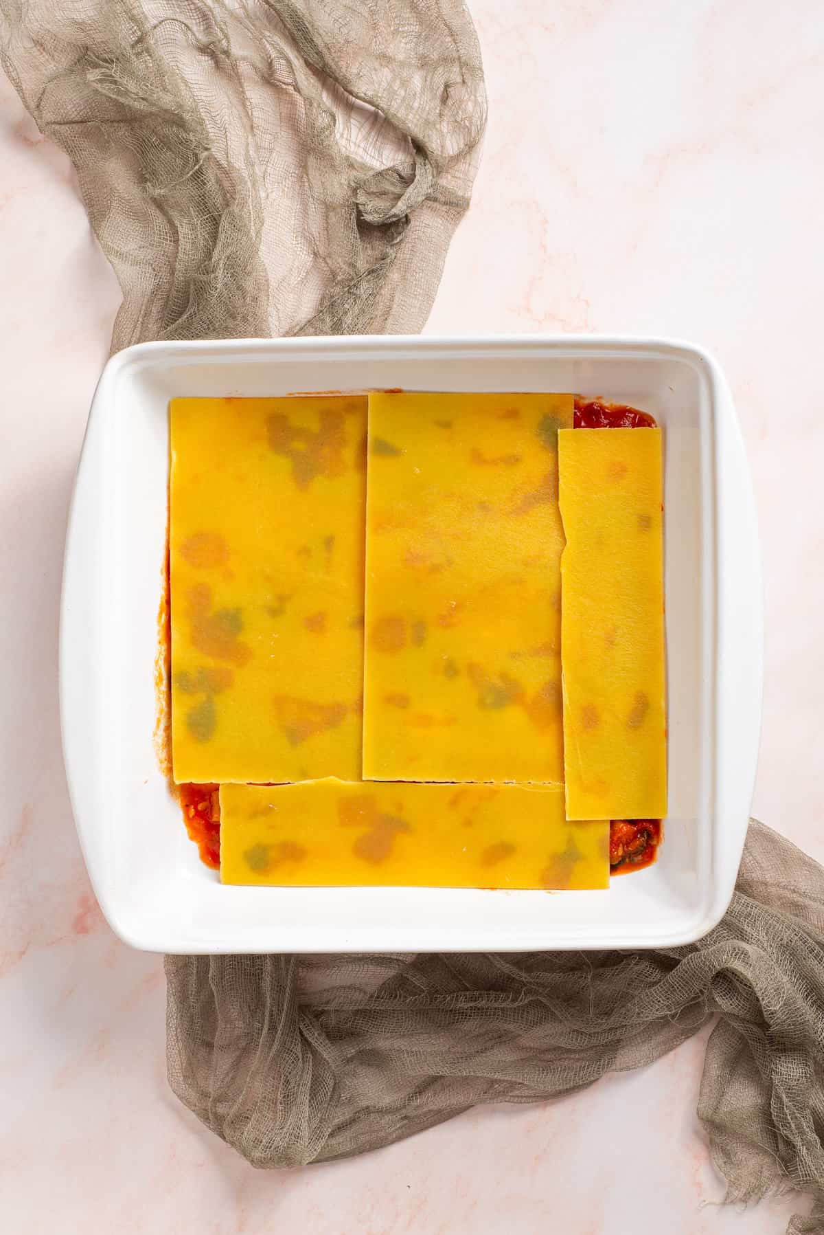 An image of the lasagna being assembled together in a baking dish, adding layer by layer.