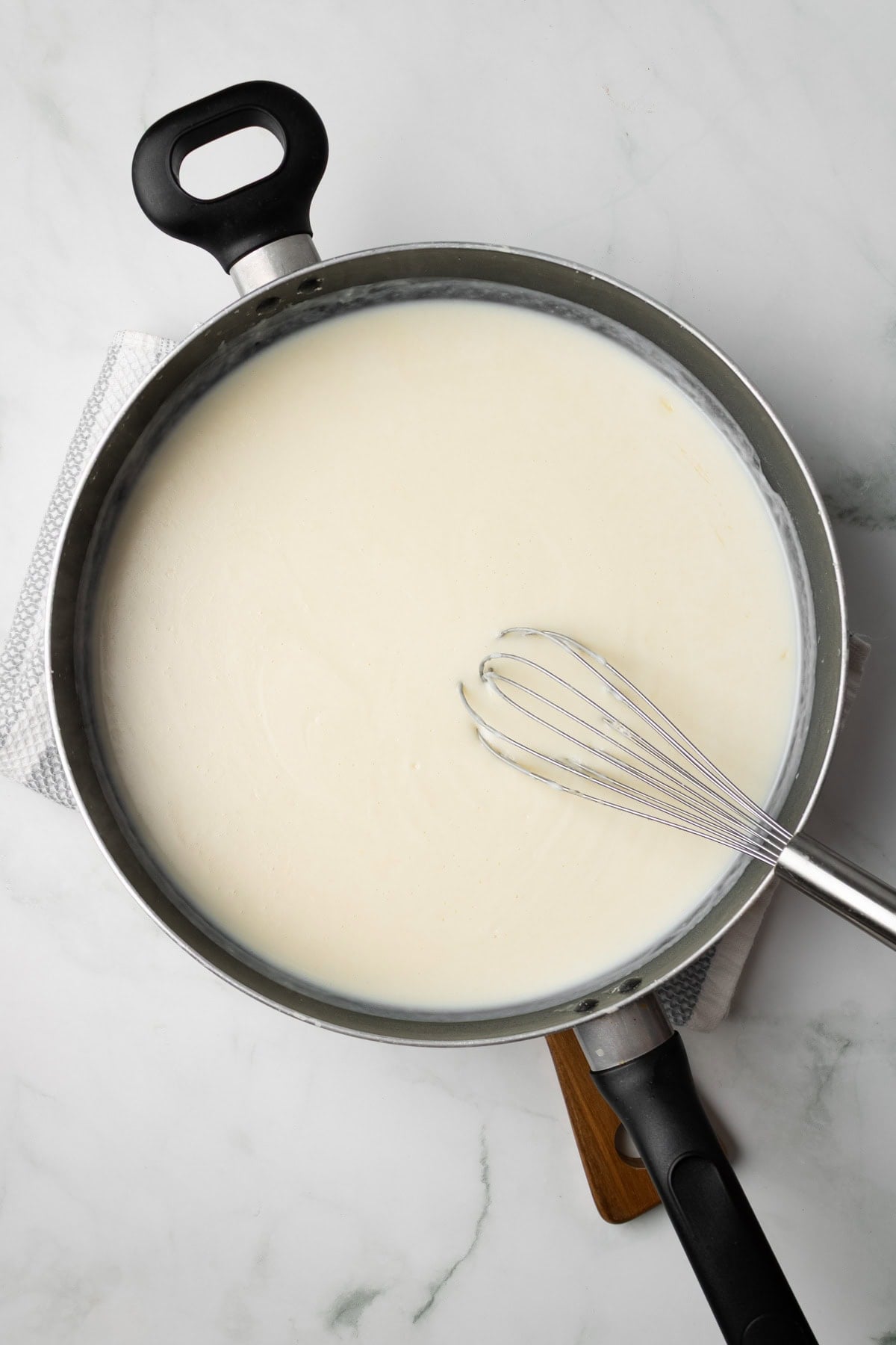 An overhead image of whisking the bechamel sauce together in a pan.