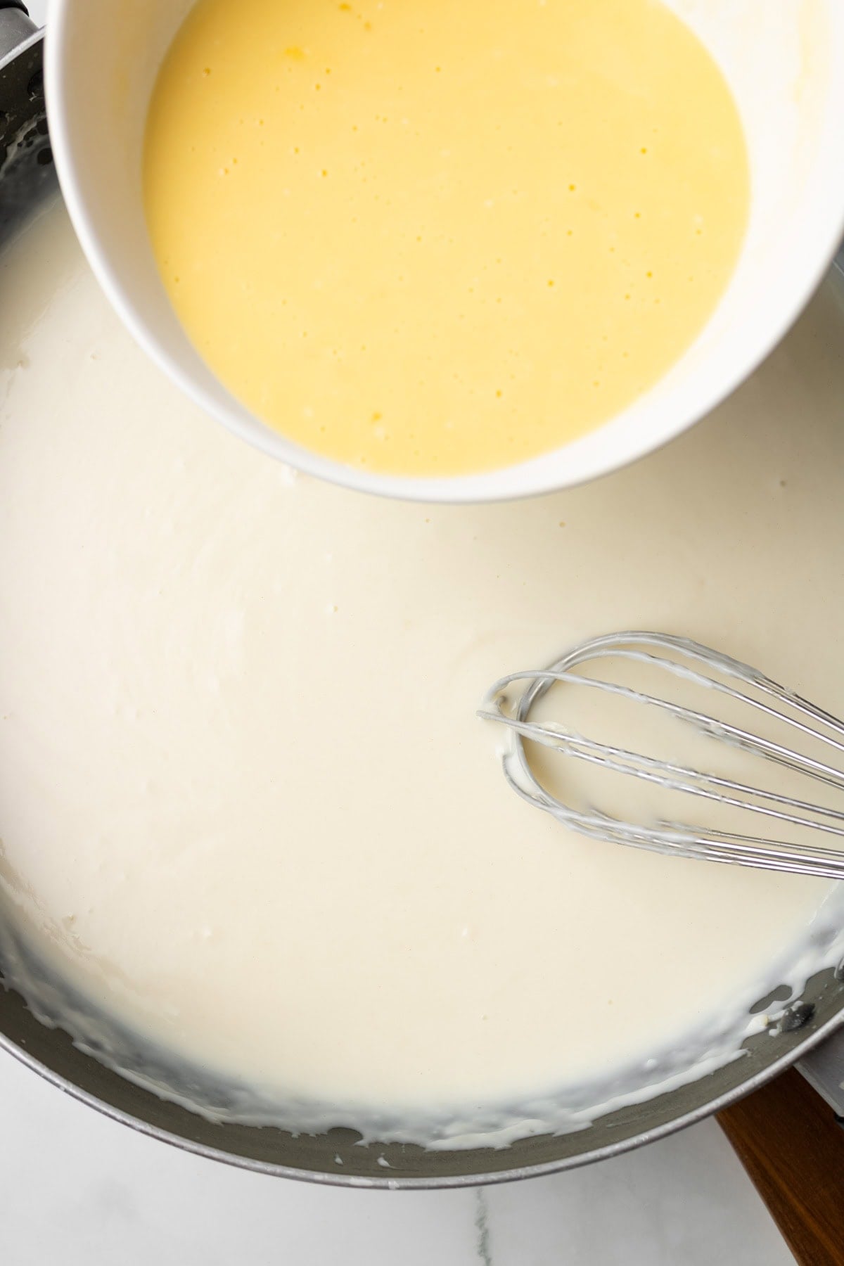 An overhead image of adding the egg mixture to the bechamel sauce.