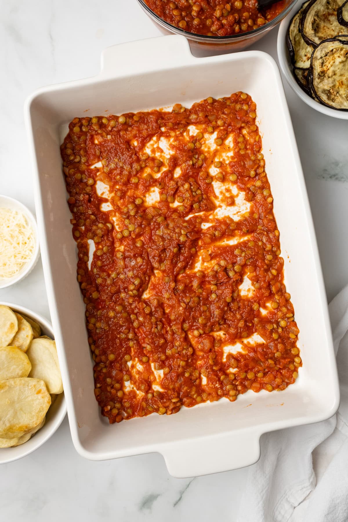 An overhead image of spreading lentil tomato sauce on the bottom of the baking dish.