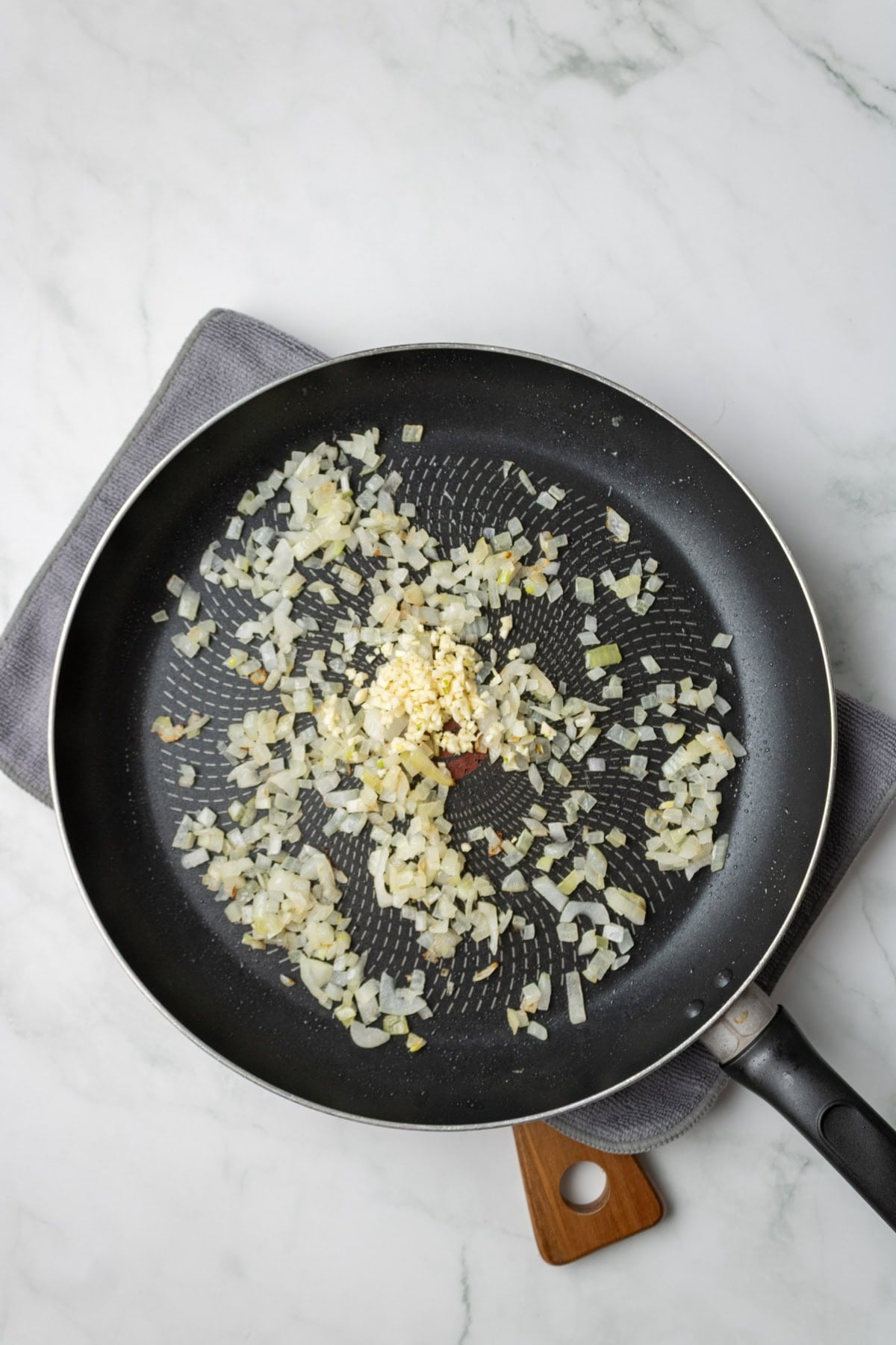 An overhead image of sauteing onions and garlic on a saucepan.