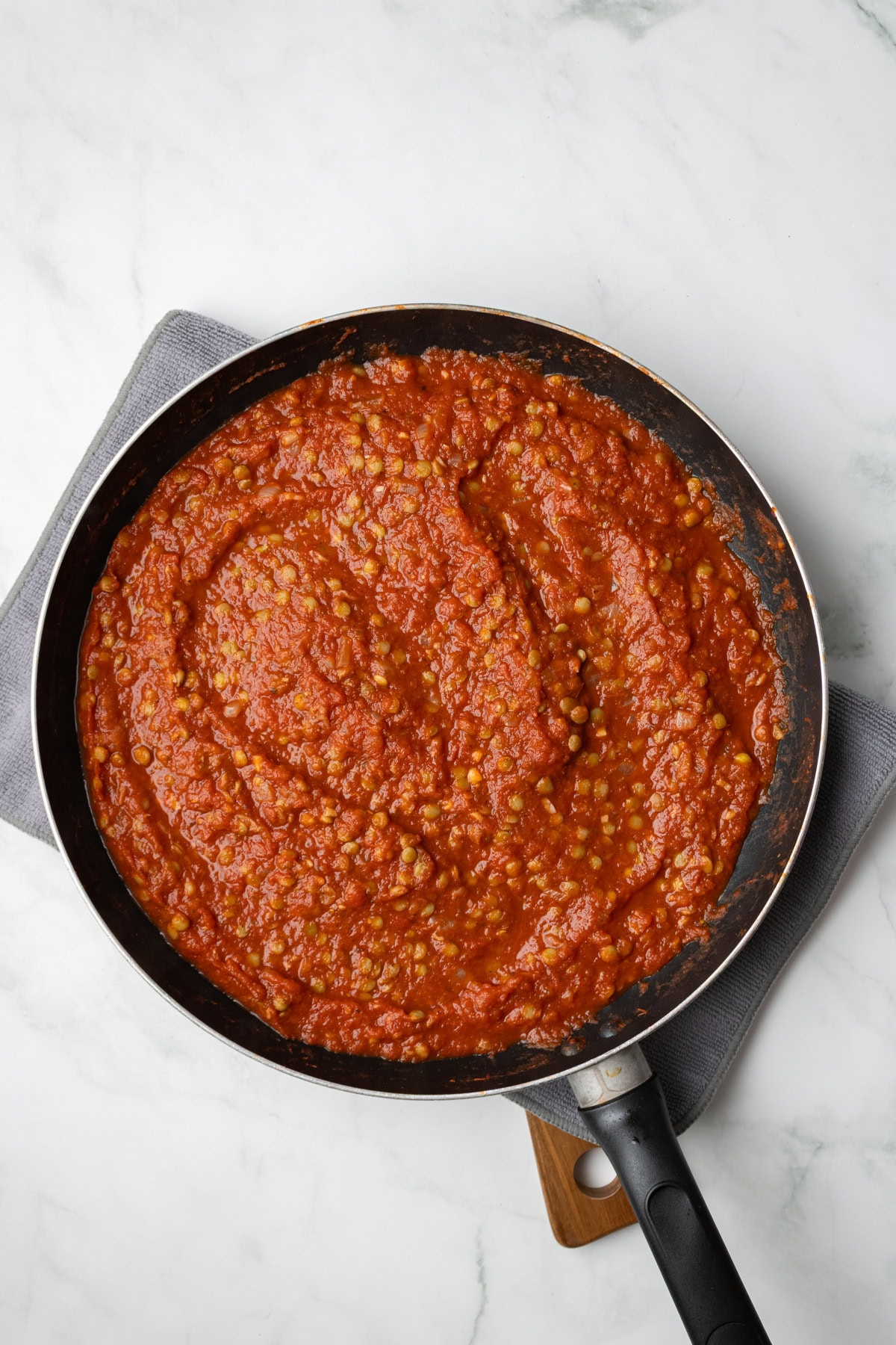 An overhead image of adding tomatoes and lentils on the saucepan.