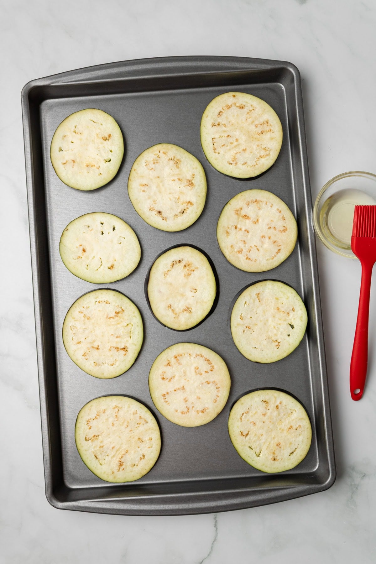 An overhead image of arranging eggplants on a baking sheet.