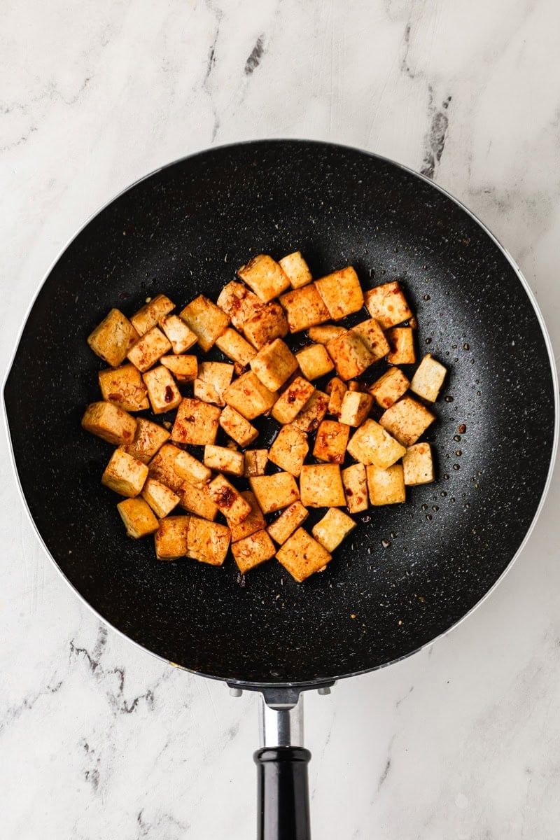 Pan-frying tofu cubes until golden brown in a wok.
