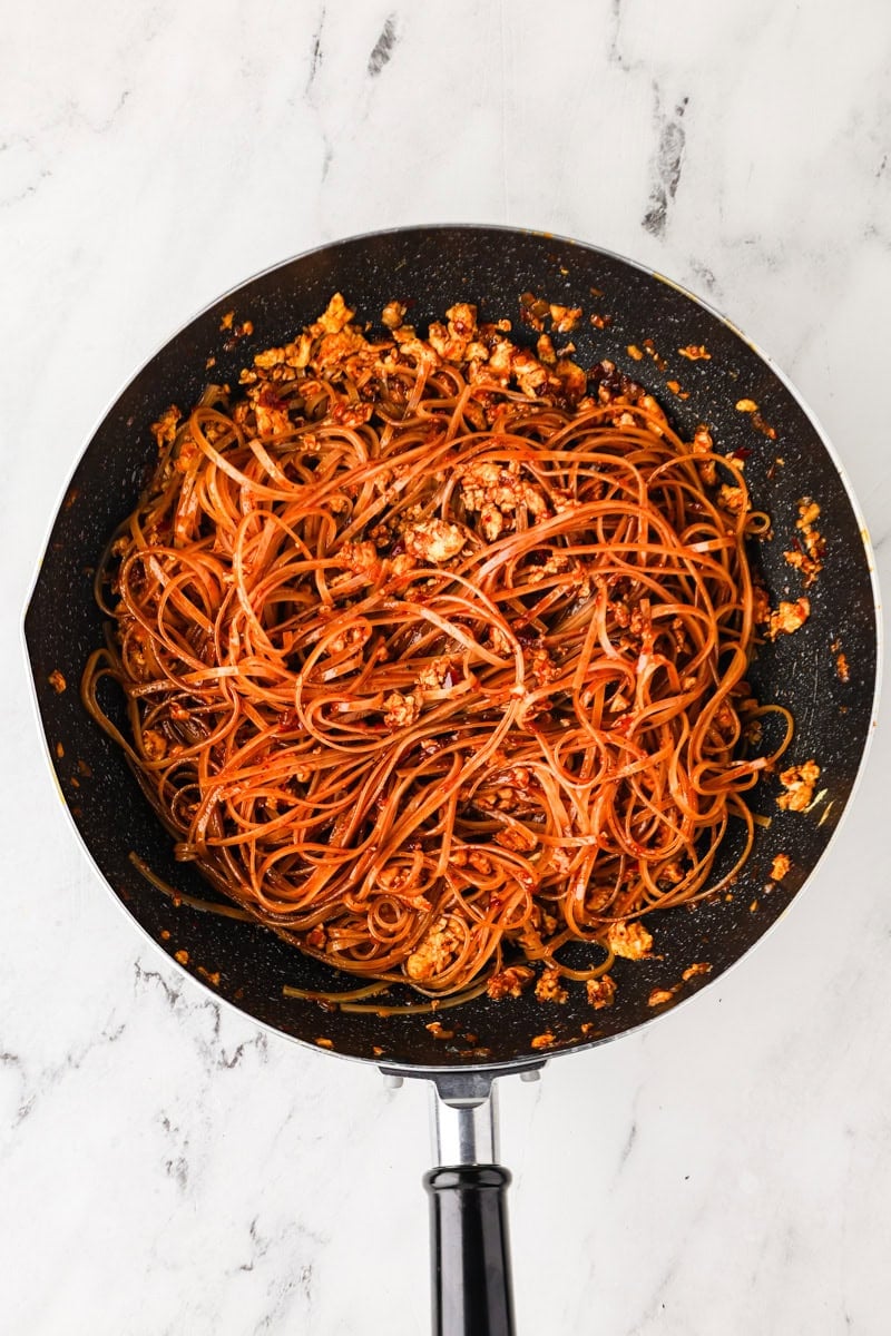 Tossing noodles with sauce in a wok for pad thai.