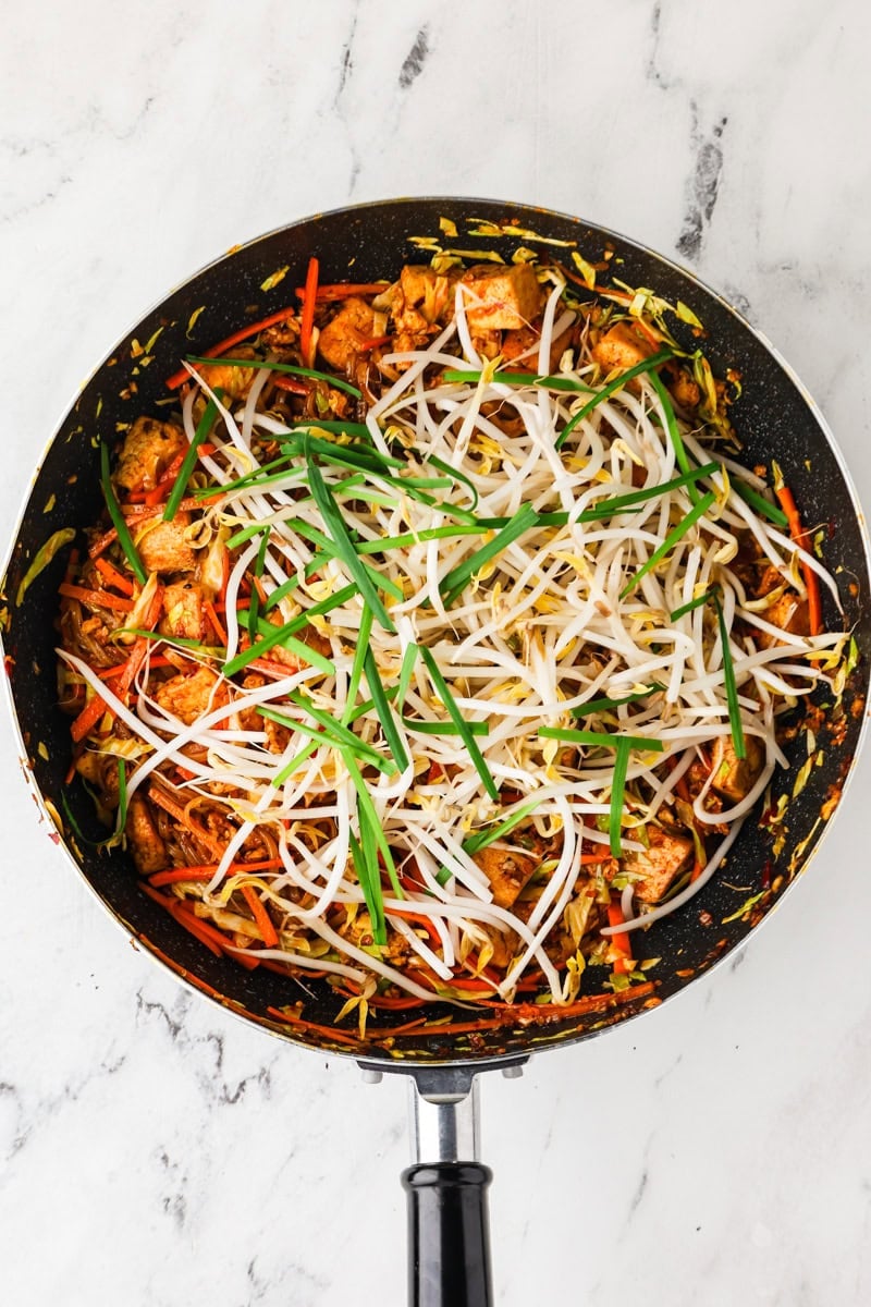 Adding vegetables and bean sprouts to tofu pad thai in wok.