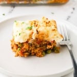 Slice of vegetarian shepherd's pie served on a white plate, showing mashed potato topping and lentil vegetable filling.