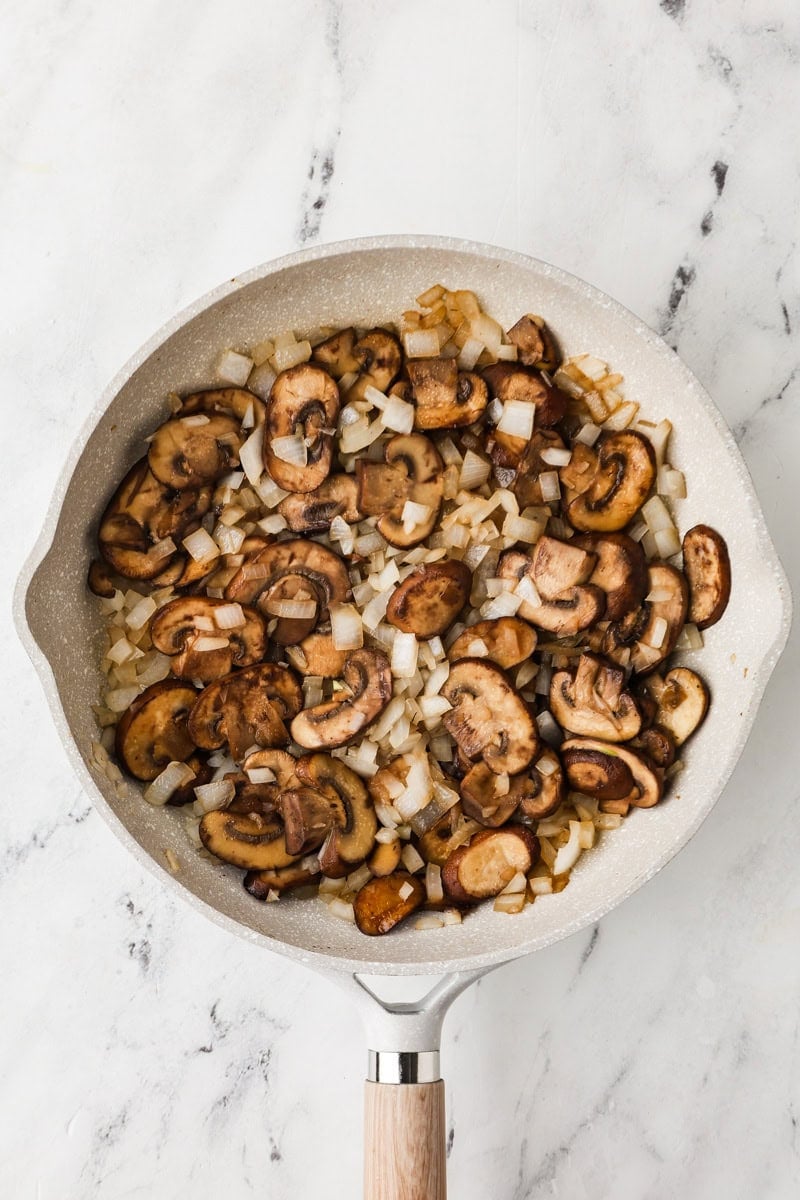 An overhead image of sauteing mushrooms and onions on a skillet.