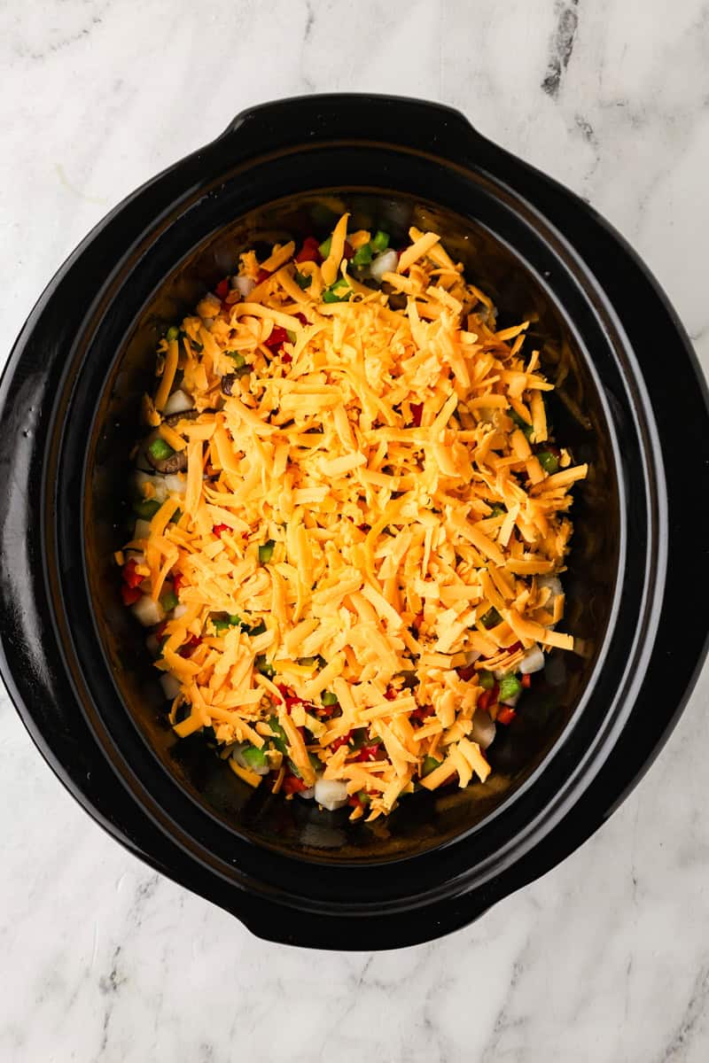 An overhead image of adding another layer of veggies, hashbrown potatoes, and cheese.