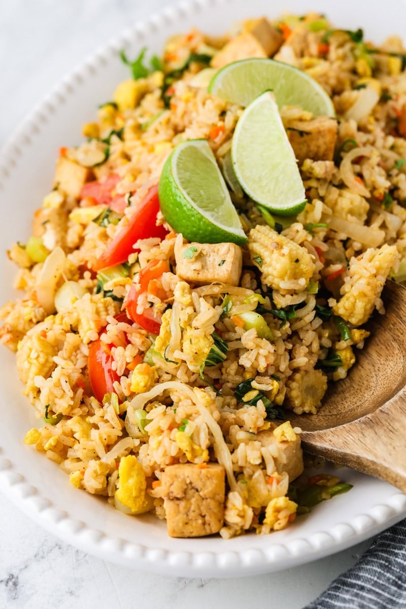 Vegetarian Thai fried rice served on an oval platter with tofu, vegetables, fresh herbs, and lime wedges.