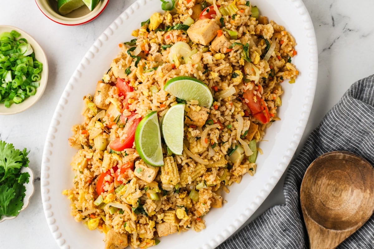 Platter of vegetarian Thai fried rice garnished with lime wedges and fresh herbs.